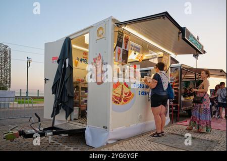 Kleiner Imbisswagen auf einem Festival, in dem bei Abendlicht Luftwaffeln und Eis für eifrige Gäste serviert werden Stockfoto