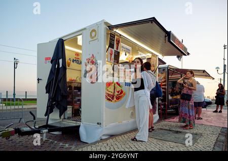 Kleiner Imbisswagen auf einem Festival, in dem bei Abendlicht Luftwaffeln und Eis für eifrige Gäste serviert werden Stockfoto