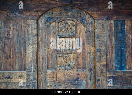 Nahaufnahme einer geschnitzten Holztür mit Szenen des alpinen Lebens im Bergdorf Dolonne, nicht weit von Courmayeur, Aosta, Italien Stockfoto