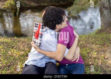 Glückliches schwules Paar, das sich in einem Park umarmt, nachdem er Geschenke an ihrem Jahrestag ausgetauscht hat Stockfoto