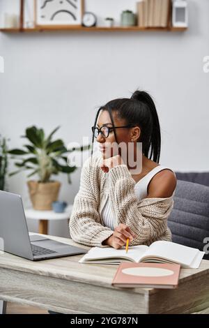 Eine schöne junge Frau konzentriert sich auf ihr Studium zu Hause, umgeben von Pflanzen und Büchern. Stockfoto