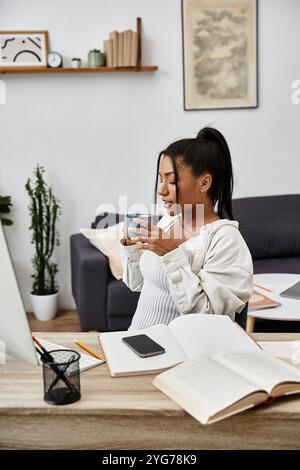 Eine junge Frau konzentriert sich intensiv auf ihre Fernstudien, während sie zu Hause Tee schlürft. Stockfoto