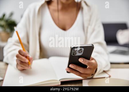 Die schöne junge Frau konzentriert sich auf ihr Studium zu Hause, indem sie ihr Handy und Notebook benutzt. Stockfoto