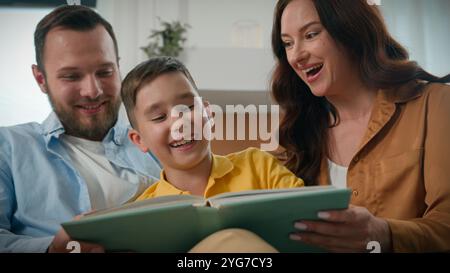 Mutter Vater Sohn liest Buch zusammen im gemütlichen Wohnzimmer liebevolle Eltern lesen Märchen Junge Kind lustig glückliche kaukasische Familie entspannend lachen Stockfoto