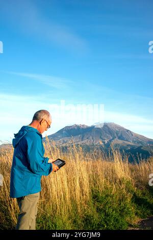 Erwachsene ältere Männer entspannen sich, während sie ein kindle-Buch mit Mount Saint Helensin im Hintergrund lesen. Northern Cascades, Bundesstaat Washington. USA Stockfoto