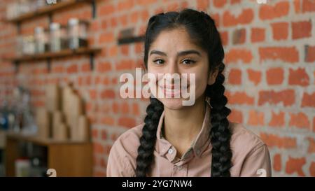 Portrait smiling indian woman waitress barista in apron posing in cafe cafeteria with crossed arms confident arabian girl female small business cafe Stockfoto