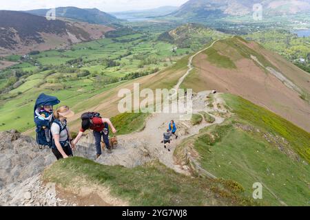 Eine Frau trägt ein kleines Baby auf dem Rücken, während sie den Gipfel der Cat Bells in Cumbria erklimmt Stockfoto