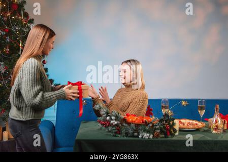 Zwei Freunde tauschen während des Weihnachtsessens Weihnachtsgeschenke mit Weihnachtsbaum, Pizza und Champagner aus Stockfoto