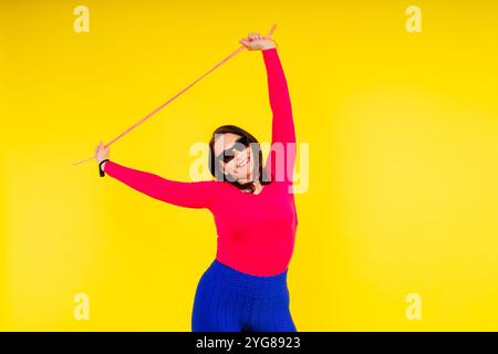 Hübsch lächelnde, pralle Frau in einem sportlichen Oberteil und Leggings, die ein Springseil in den Händen hält Stockfoto