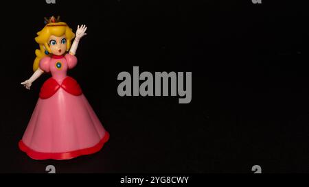 Prinzessin Peach steht auf der linken Seite eines schwarzen Hintergrunds, Prinzessin Peach Toadstool Plastikfigur mit Kopierraum, Animationstag, Spieltag Stockfoto