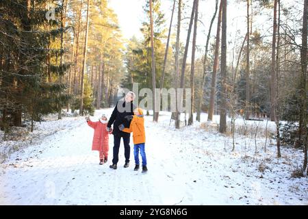 Ein Vater macht einen gemütlichen Spaziergang mit seinen beiden Kindern durch einen wunderschönen verschneiten Wald. Die Szene fängt die Freude der Familie in der ruhigen W ein Stockfoto