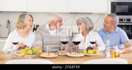 Zwei ältere Ehepaare sitzen am Tisch, genießen Essen und Wein, plaudern. Stockfoto