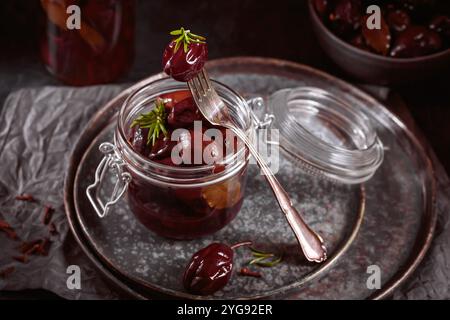 Marinierte Pflaumen mit Gewürzen im Glasgefäß auf dem Küchentisch Stockfoto