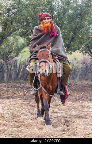 Khan Sahib Tehsil, Jammu und Kaschmir, Indien. Mann mit rotem Henna-gefärbtem Bart, der auf einem Pferd reitet. Stockfoto