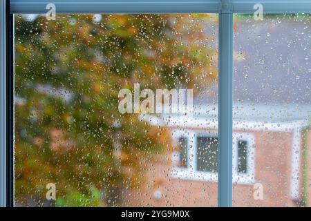 An einem regnerischen Herbsttag in Basingstoke treffen Regentropfen ein Fenster mit wechselnden Blättern und einem Vorstadthaus dahinter. Konzept: montag-Feeling Stockfoto