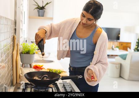 Asiatische Frau kocht in der Küche, gießt Soße in Wok, bereitet Mahlzeiten zu Hause vor Stockfoto