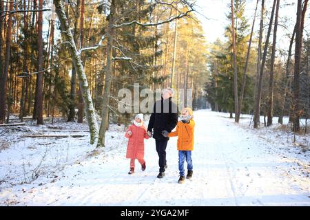 Ein Vater macht einen gemütlichen Spaziergang mit seinen beiden Kindern durch einen wunderschönen verschneiten Wald. Die Szene fängt die Freude der Familie in der ruhigen Winterlandschaft mit schneebedeckten Bäumen ein, die eine magische Kulisse bilden. Stockfoto
