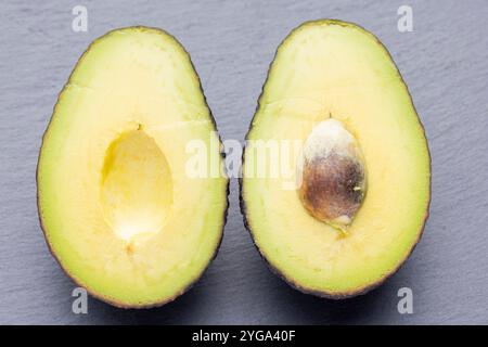 Ein Nahaufnahme von zwei Avocadohälften, eine davon mit intakter Grube, auf einer grauen Oberfläche. Das Avocadofleisch ist ein leuchtendes Gelbgrün und das Stockfoto