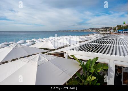 Nizza, Frankreich - 24.09.2024: Auswahl an weißen Sonnenschirmen über dem Restaurant am sonnigen Sommermorgen mit Mittelmeer im Hintergrund. Stockfoto