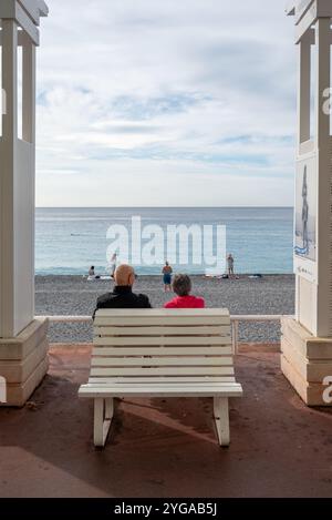 Nizza, Frankreich - 24.09.2024: Seniorenpaar sitzt am sonnigen Sommermorgen auf einer Bank mit Blick auf das Mittelmeer und den Strand an der Promenade des Anglais. Stockfoto