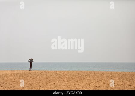 Ouidah, Benin. Januar 2022. Gegenüber dem Platz, der dem Voodoo-Festival in Ouidah, Benin, zugewiesen ist, spaziert ein junger Straßenverkäufer am Strand auf und ab. Jedes Jahr am 10. Januar findet in Ouidah, Benin, ein Voodoo-Festival statt, um die Gottheiten dieser westafrikanischen Religion zu feiern, in der Nähe des Gate of No Return, das an die Deportation von Millionen Gefangenen während des Sklavenhandels erinnert. Die in Benin geborene Vodun- oder Voodoo-Religion stammt aus animistischen Traditionen und basiert auf der Verbindung mit der Natur und den Vorfahren. (Foto: Apolline Guillerot-Malick/SOPA Images/SIPA USA) Credit: SIPA USA/Alamy Live News Stockfoto