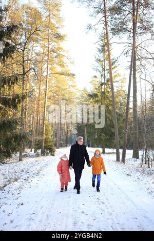 Ein Vater macht einen gemütlichen Spaziergang mit seinen beiden Kindern durch einen wunderschönen verschneiten Wald. Die Szene fängt die Freude der Familie in der ruhigen Winterlandschaft mit schneebedeckten Bäumen ein, die eine magische Kulisse bilden. Stockfoto