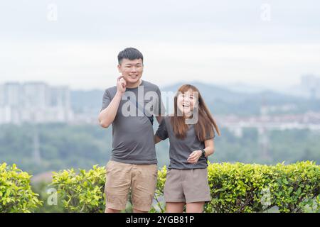 Ein chinesisch-malaysisches Paar in den 30ern, das an einem sonnigen Jun-Tag in Kuala Lumpur, Malaysia, auf einem malerischen Hügel in einem grünen Park mit reichlich Wasser steht Stockfoto