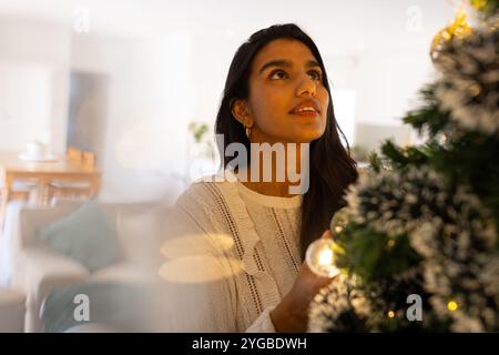 Weihnachtsbaum dekorieren, asiatische Frau, die Lichter zu Hause bewundert, festlich fühlt Stockfoto