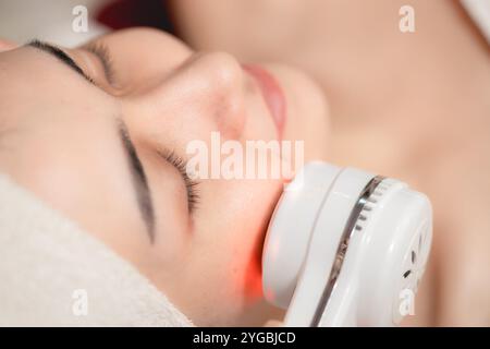 Gesichtskosmetik mit Ultraschall-Laser-Hautglühen-Verfahren. Junge Frauen sehen sich der Skin Spa-Technologie gegenüber. Stockfoto