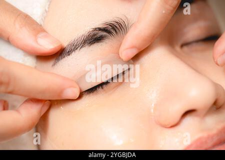 Lidbehandlung. Anti-Aging-Klinikfrau schloss Augen mit Gel zur Behandlung des Oberlids. Masseurin sanfte Massage Gesicht und Augen des Kunden Stockfoto