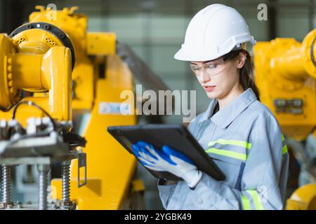 Ingenieurin, die in einer Maschinenfabrik arbeitet. Ingenieurinnen arbeiten mit dem Prüfen des Roboterarms im Montagewerk mit Tablet Stockfoto