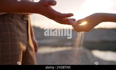 Ein Paar, das bei Sonnenuntergang Sand aus den Händen gießt, was Zeit, Verlust und die vergängliche Natur des Lebens repräsentiert Stockfoto