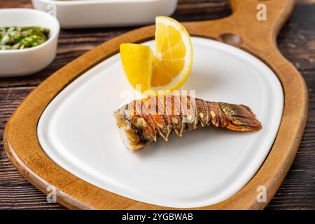 Gegrillter Hummerschwanz auf weißem Porzellanteller auf Holztisch mit Zitrone Stockfoto