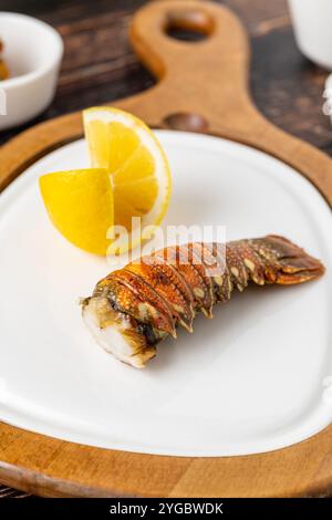 Gegrillter Hummerschwanz auf weißem Porzellanteller auf Holztisch mit Zitrone Stockfoto