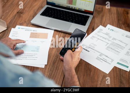 Der Finanzspezialist von man nutzt das Smartphone, um die Gesamtrechnungen von Versorgungsunternehmen am Arbeitsplatz zu zählen Stockfoto