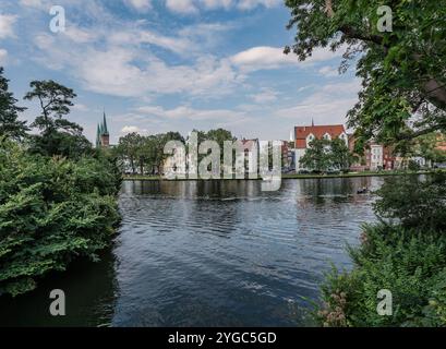 Ein ruhiger Blick auf die historische europäische Architektur an einem ruhigen Fluss, umgeben von üppigem Grün. Das Bild fängt die Schönheit der Natur und den urbanen Charme ein Stockfoto