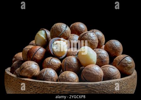 Macadamia-Nüsse mit Schalen in Schüssel auf schwarzem Hintergrund, Nahaufnahme Stockfoto