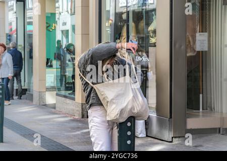 Wie man in der eigenen Handtasche sucht. Eine stilvolle junge Frau hält auf dem Bürgersteig an, um durch ihre Handtasche zu schauen. Stockfoto