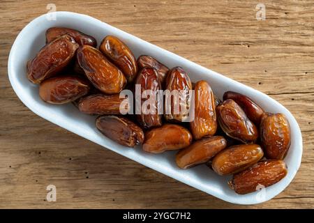 Trockene Datteln Obst in einem weißen Behälter auf hölzernem Hintergrund, Draufsicht, Nahaufnahme Stockfoto