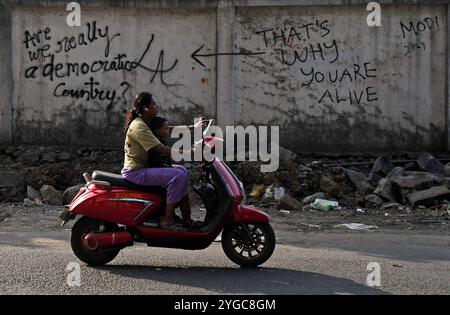 Das tägliche Leben in Mumbai, Indien eine Inderin und ein Kind fahren mit einem Roller an Graffiti-Nachrichten vorbei, die am 06. November 2024 in einer Straße in Mumbai, Indien, an einer Wand gemalt wurden. Graffitis werden im öffentlichen Raum ohne Erlaubnis gemalt, um soziale und politische Szenarien in der Gesellschaft zu beschreiben. Mumbai Indien Copyright: XMatrixxImagesx/xStringerx Stockfoto