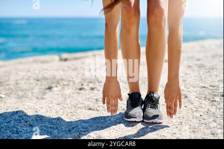 Frau, Beine und Stretching mit Händen am Strand für Fitness, Sport oder Aufwärmen auf Felsen in der Natur. Weibliche Person, Füße oder nach Zehen greifen, Workout Stockfoto