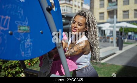 Frau mit Tätowierungen spielt mit Tochter auf dem Spielplatz im urbanen Outdoor Park an einem sonnigen Tag Stockfoto