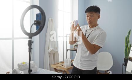 Junger Mann, der im Spa-Setting Videos aufnimmt, mit Mobiltelefon, das Produkt- und Ringlicht zeigt und die Schönheit und Entspannung in Innenräumen betont. Stockfoto