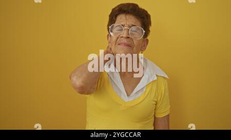 Ältere hispanische Frau mit kurzen Haaren und Brille, in gelber Kleidung, auf einem isolierten gelben Hintergrund stehend, reflektierend und tou Stockfoto