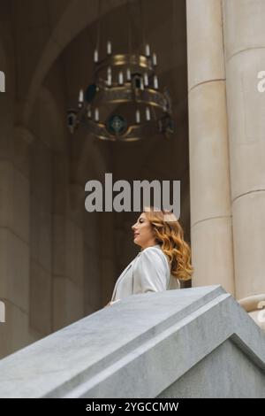 Frau Kronleuchter Treppe - Blonde Frau blickt nach oben auf einen Kronleuchter, während sie auf einer großen Treppe steht. Stockfoto