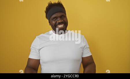 Hübscher afroamerikanischer Mann mit Bart und Stirnband, der selbstbewusst vor gelbem Hintergrund lächelt. Stockfoto