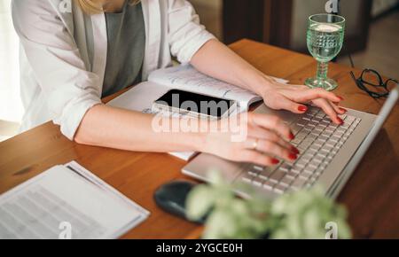 Komfort trifft auf Funktionalität im Home Office-Setup, Frauenhände mit einem Laptop am Tisch bei der Arbeit Stockfoto