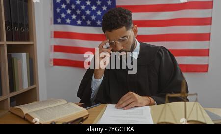 Junger Mann im Richtergewand, der Dokumente im Amt liest, mit amerikanischem Flaggenhintergrund Stockfoto