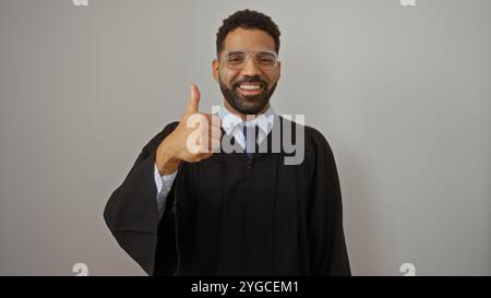 Hübscher junger hispanischer Mann im Abschlusskleid, der Daumen hoch über weißem Hintergrund hält Stockfoto