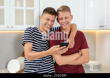 Glückliche Brüder, die in der Küche auf das Smartphone schauen Stockfoto